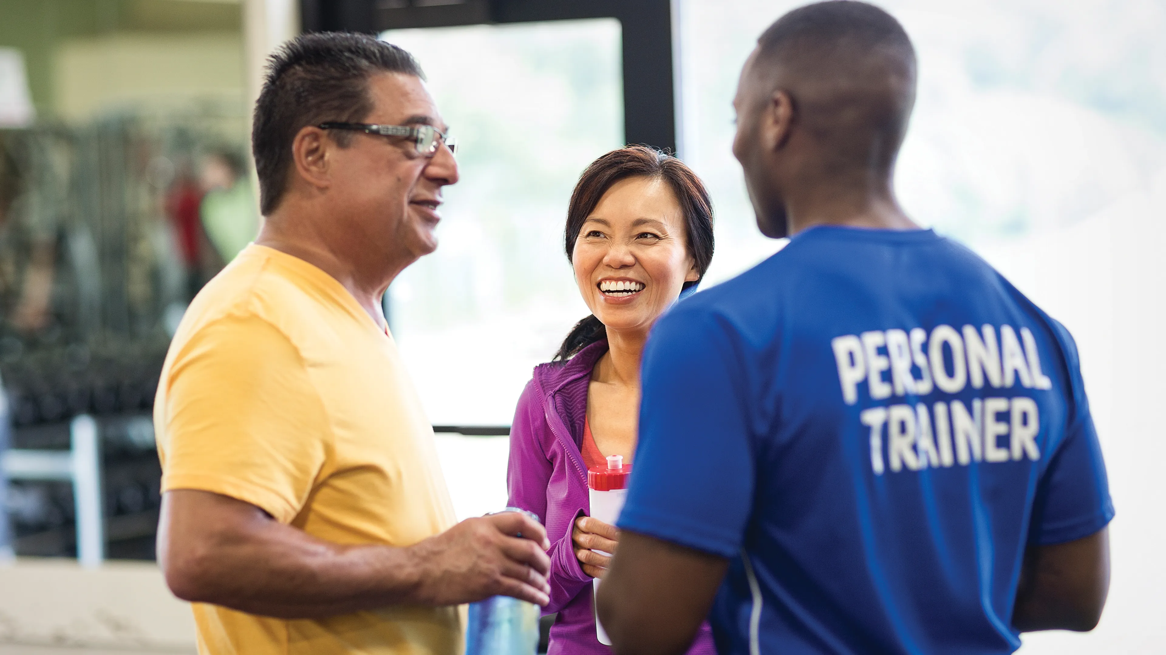 Male personal trainer talking with a man and a woman